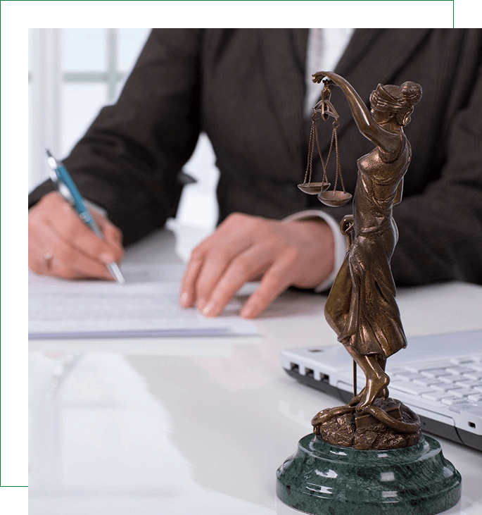 A person writing on paper near a statue of lady justice.